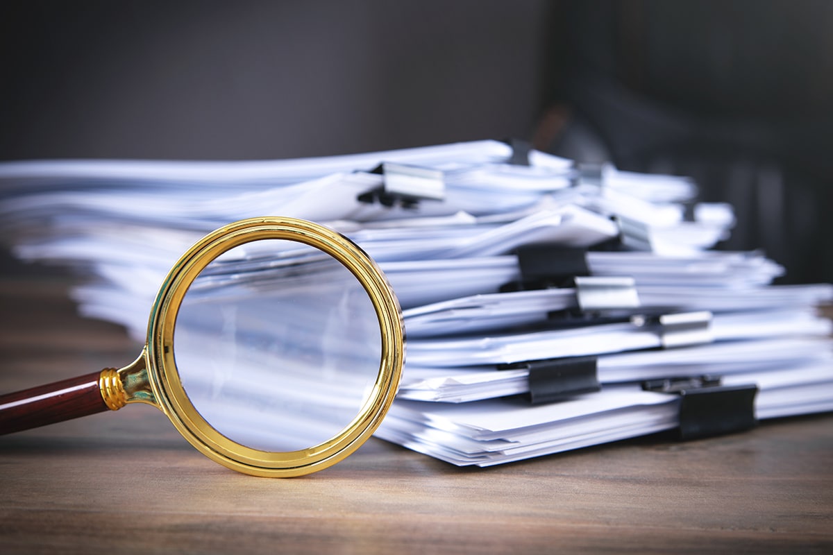 A stack of financial papers with a magnifying glass